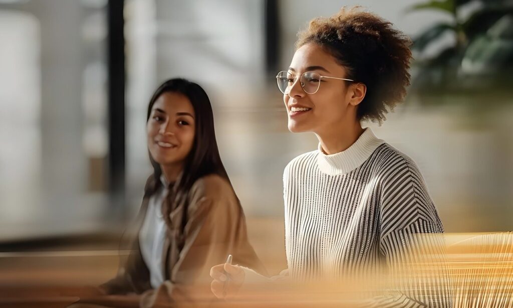 Dos mujeres en un entorno de aprendizaje moderno, participando activamente en una formación sobre inteligencia artificial. Representación del programa AI Skills 4 Women.