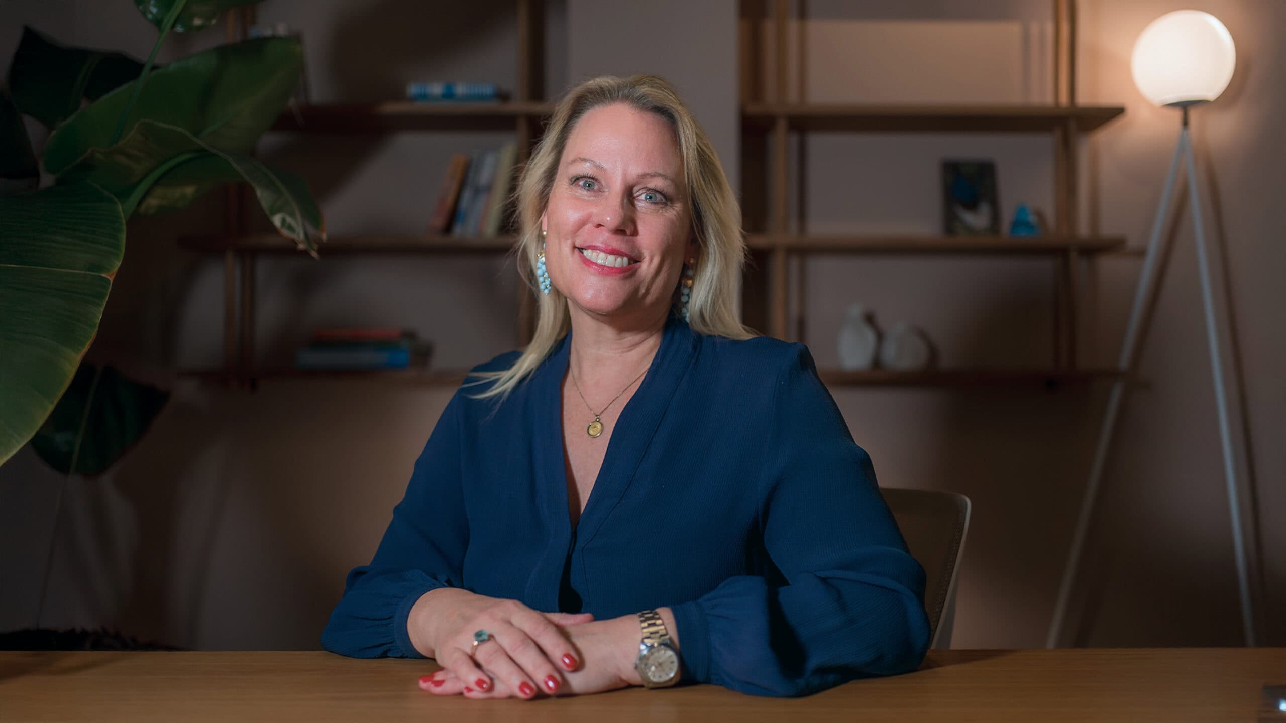 Andrea Fogel smiling at a desk in a blue blouse, shelves behind