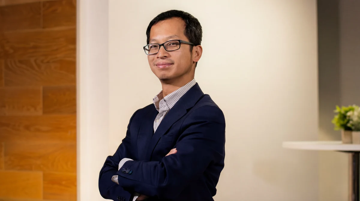 Benny Lee smiling with arms crossed, wearing glasses and a navy blazer