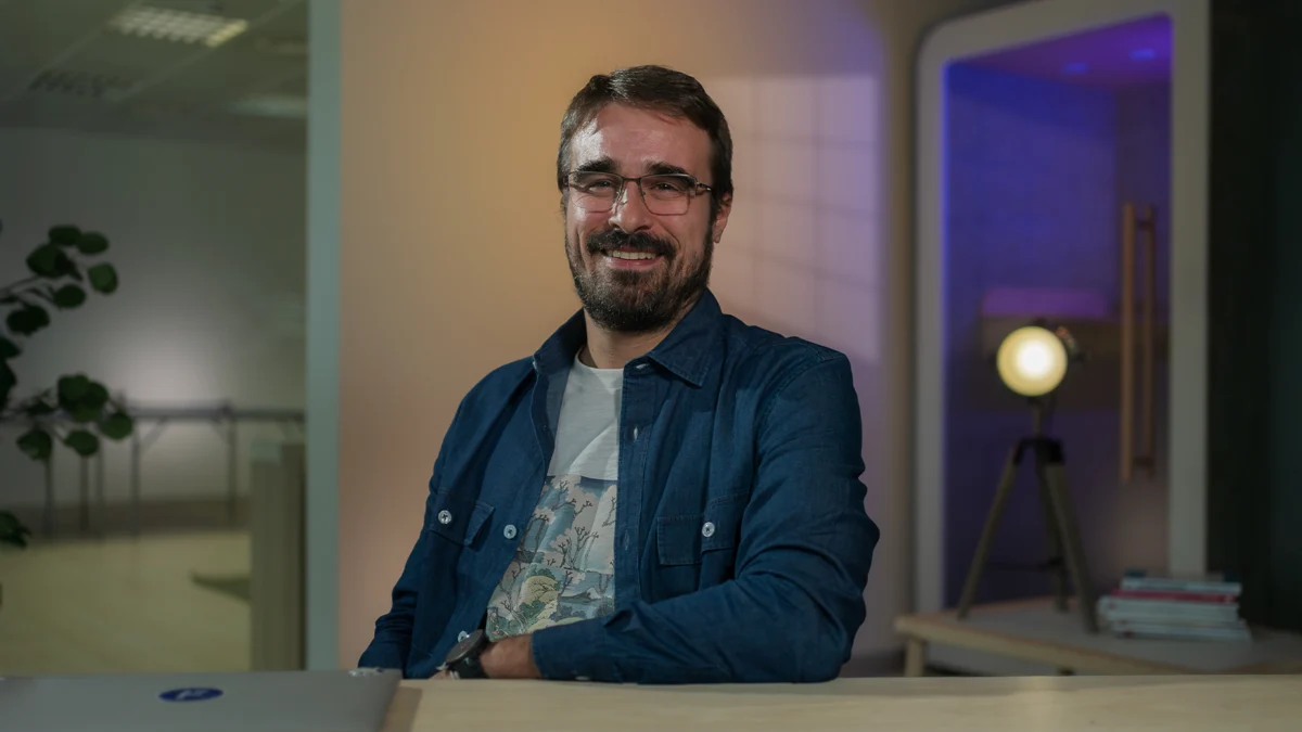 David Sierra smiling in glasses and denim shirt at a desk