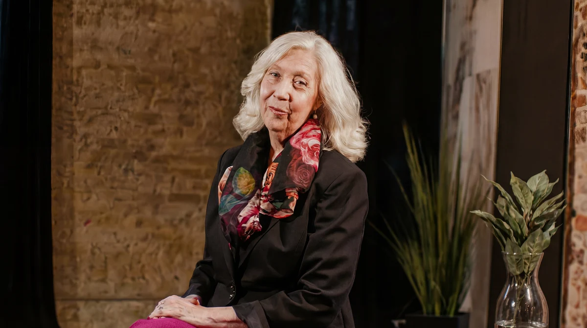 Deanna Leonard seated in a black blazer and floral scarf, smiling