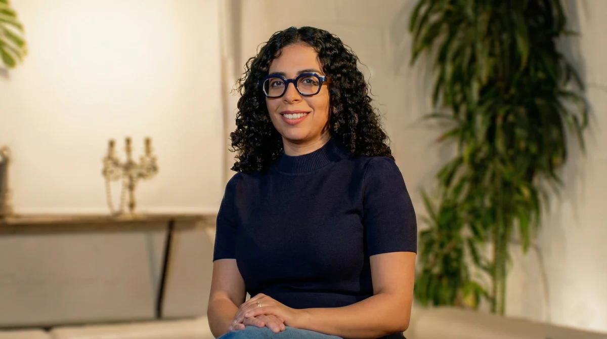 Ilham Bazi smiling, seated with glasses and navy top, plants behind