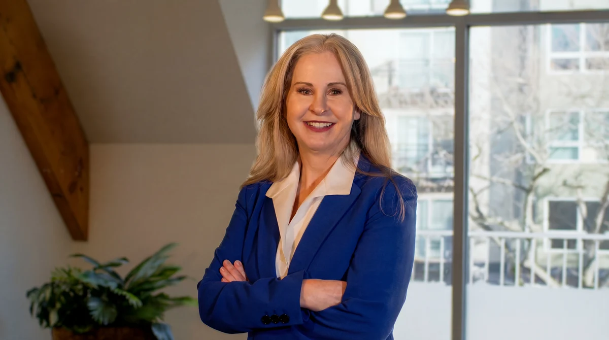 Megan Clarke smiling in a blue blazer, arms crossed, by a bright window