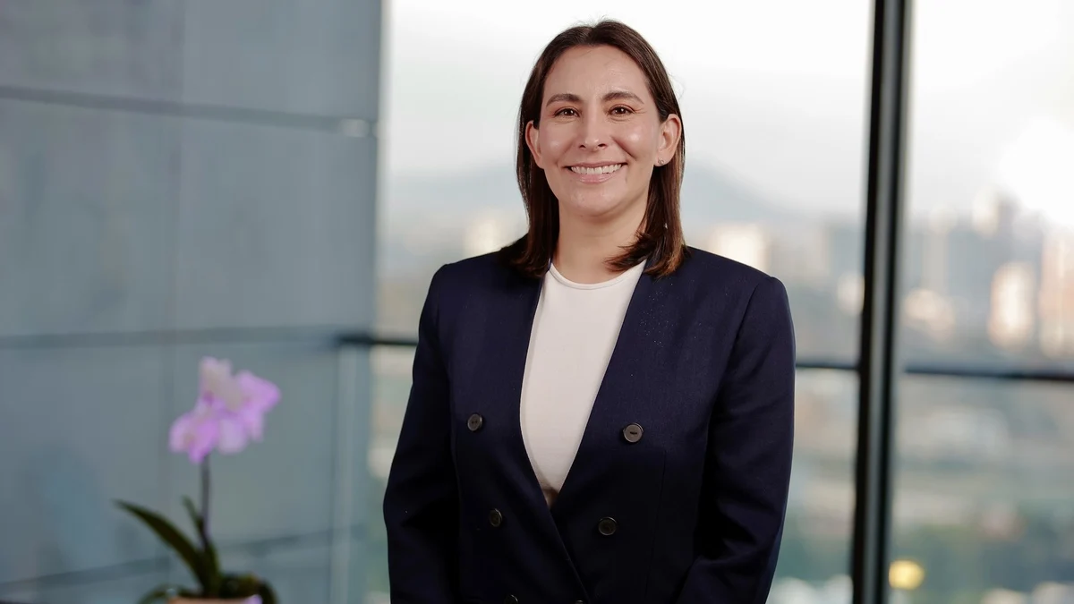 Paola Parra smiling in a navy blazer beside an orchid and city view