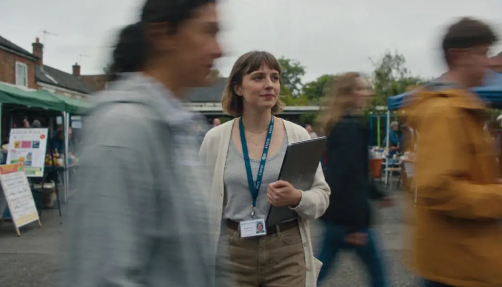 Woman with lanyard badge carrying a laptop through a busy outdoor market