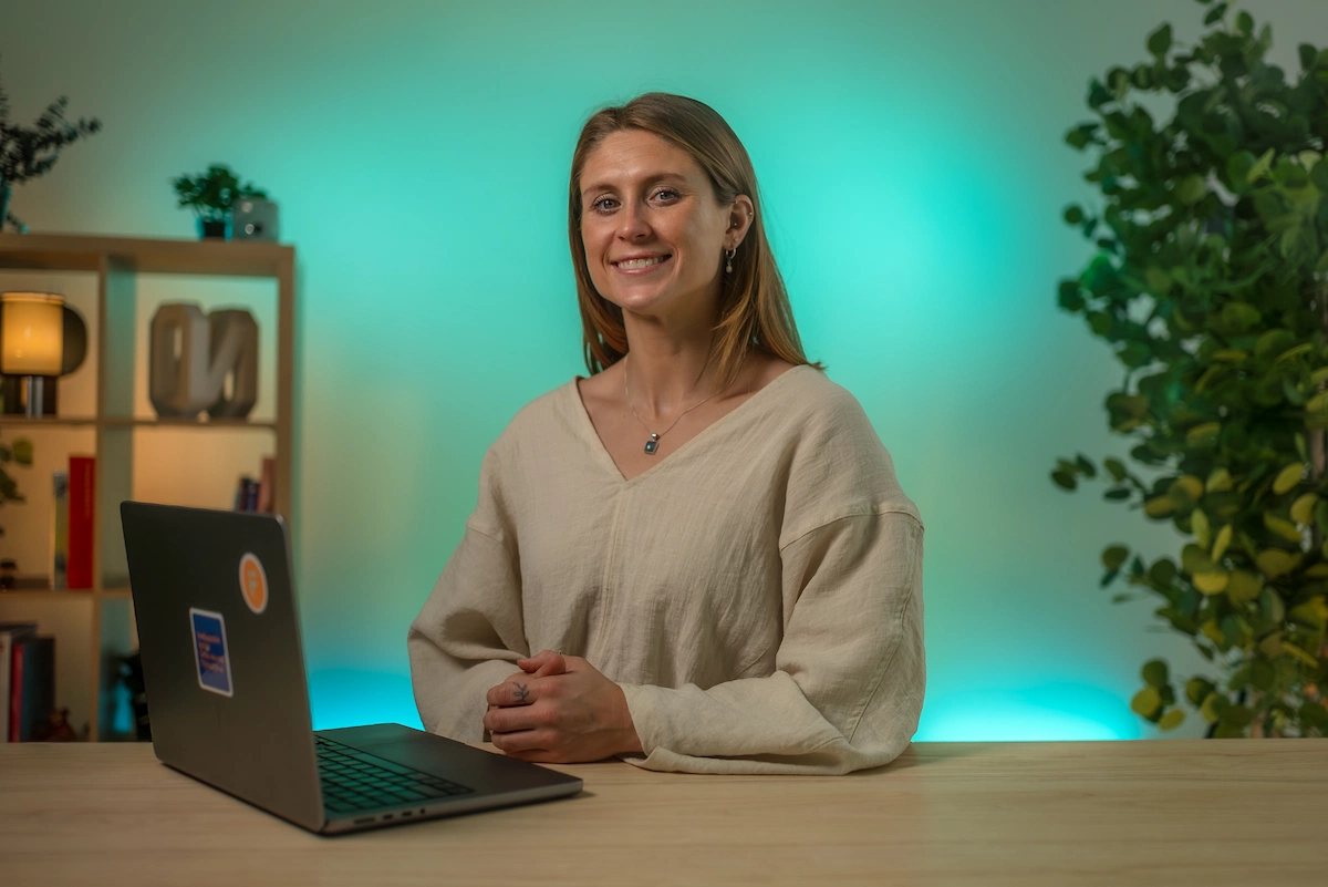 Anna Ogan smiling at a desk with a laptop against teal lighting