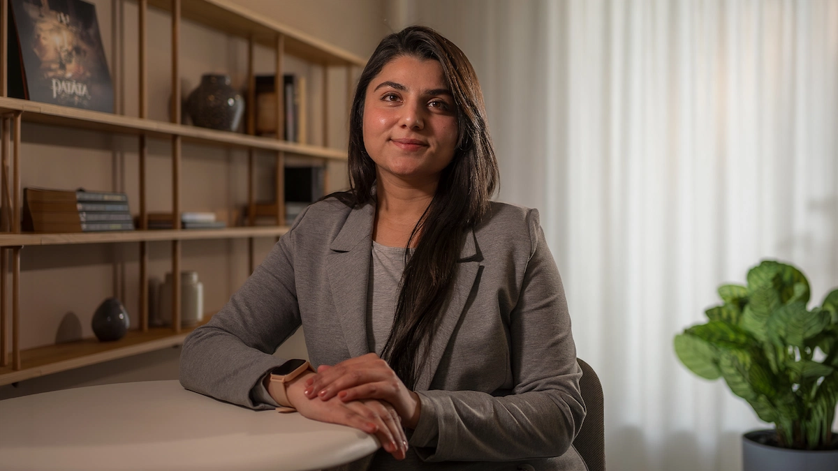 Nida Fareed in a grey blazer seated at a desk, smiling