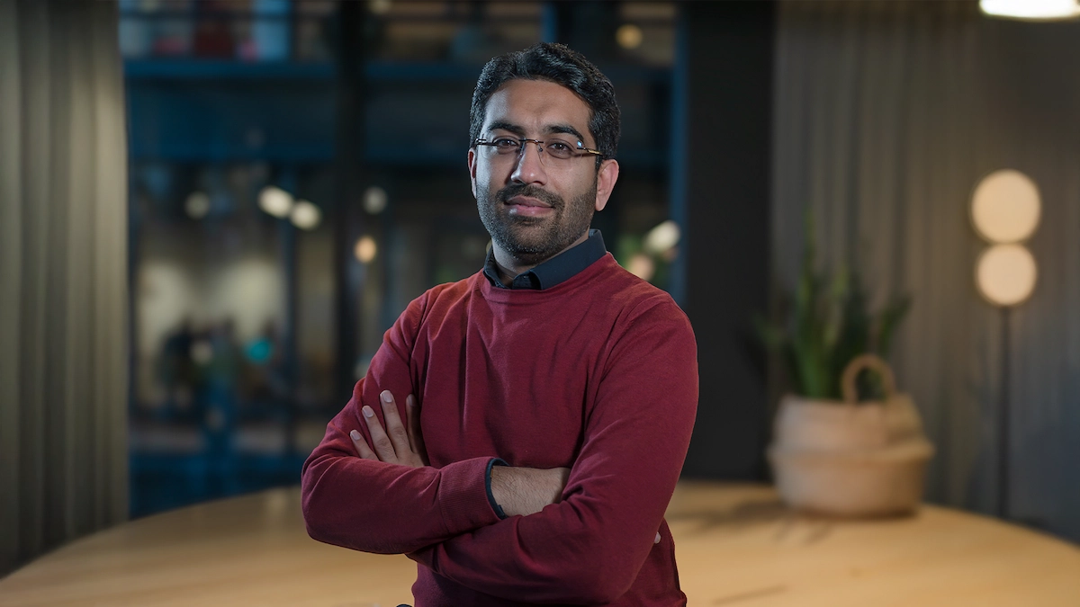 Usman Afzal in a red sweater with arms crossed in an office